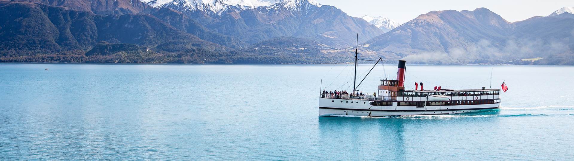 The historic TSS Earnslaw Steamship cruises along Lake Wakatipu with a view of The Remarkables mountain range 