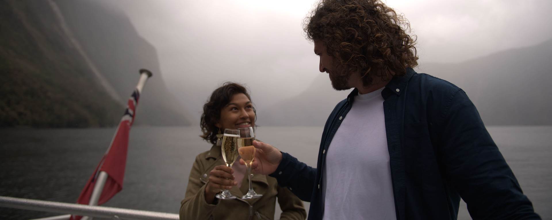 A couple clinking champagne glasses on Milford Sound