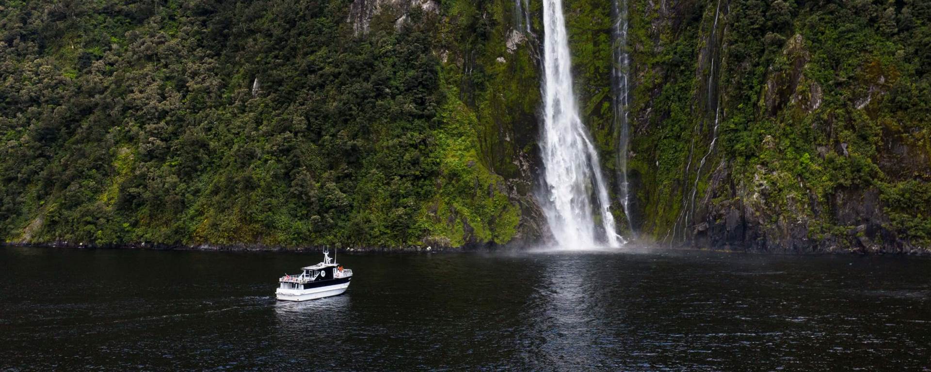 Boat in milford sound approaching waterfall